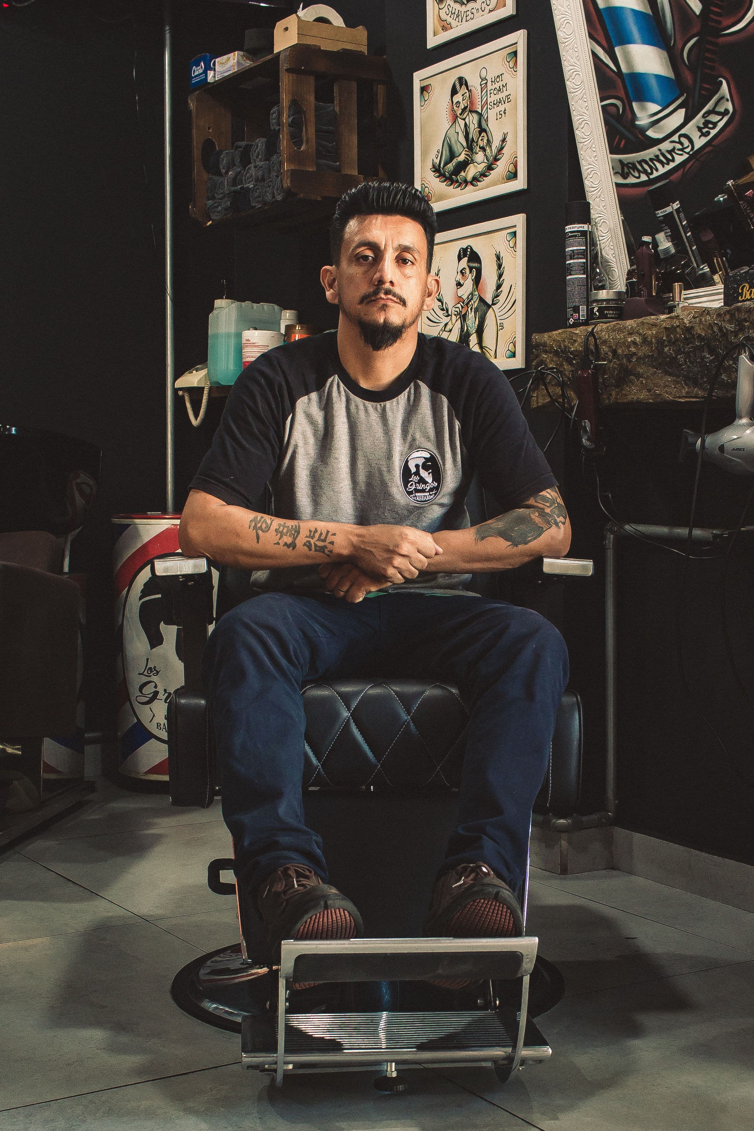 Portrait of barber Mateo with a goatee and tattooed forearms, seated in a leather barber chair