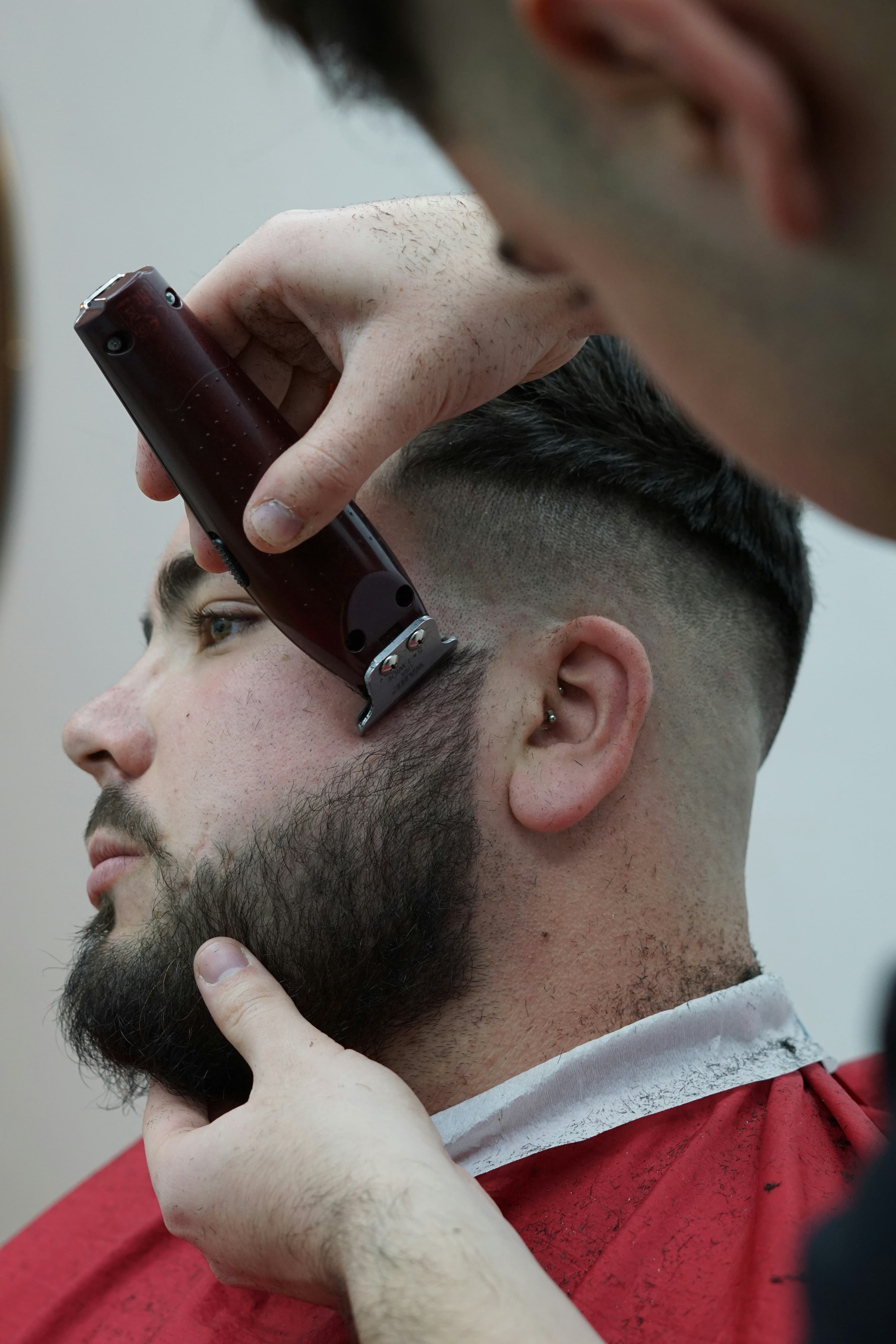 Barber shaping a client’s full beard with a red cordless trimmer