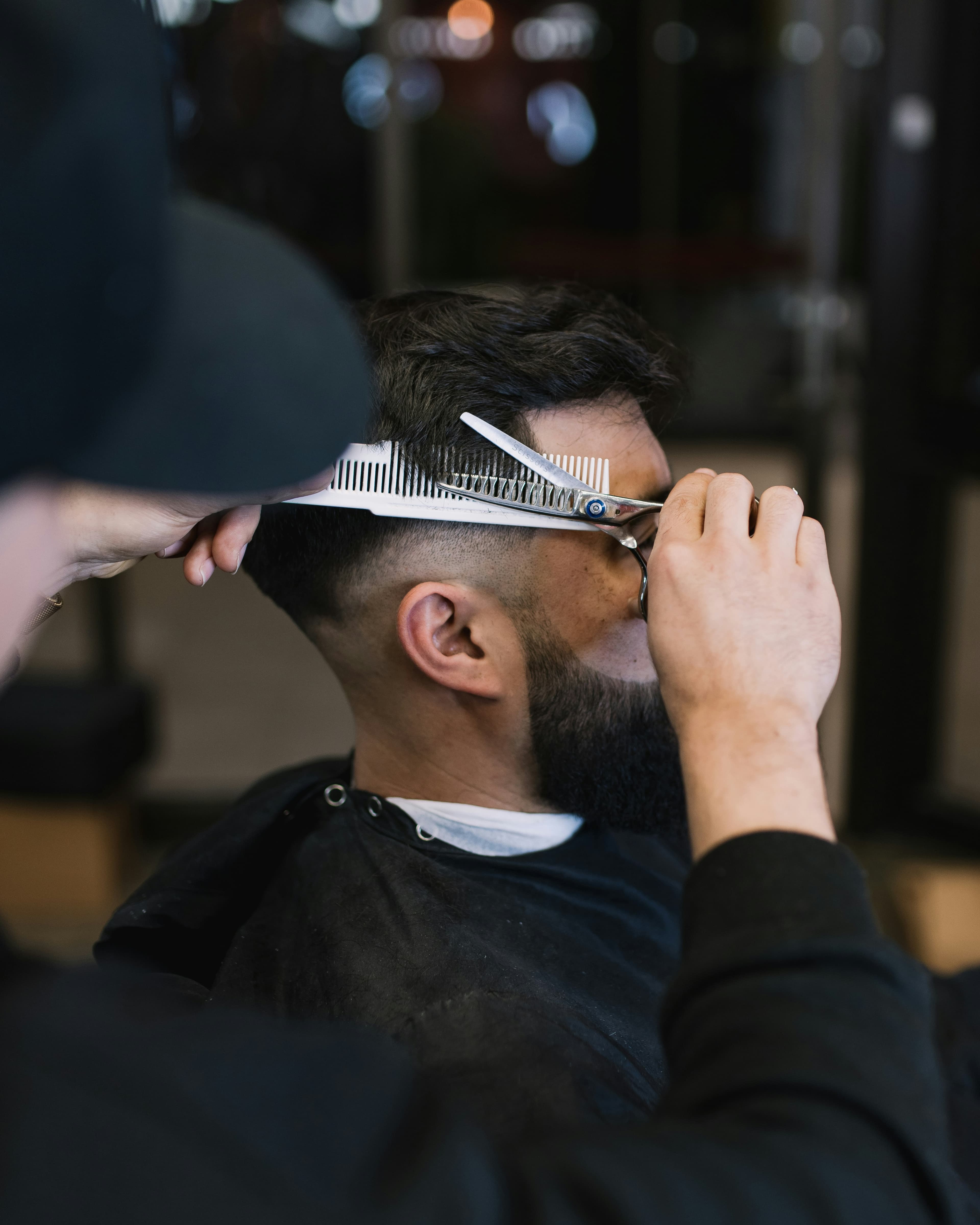 Barber cutting a client’s hair with scissors and a comb above a skin fade